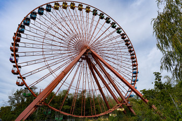 old abandoned red ferris wheel with colorful gondolas in sunny weather and blue sky
