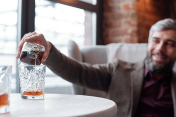 Close-up of happy man pouring whisky into glass while resting in lounge bar