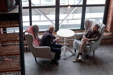 Above view of stylish middle-aged businessmen sitting in comfortable armchairs and drinking alcohol in lobby bar