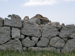 An ancient fence made of huge stones in the mountains of Crimea against the blue sky with white Cumulus clouds on a Sunny summer day.