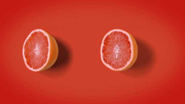 Stop motion minimal animation Top view on grapefruit halves rotating, wiggling or dancing on orange background. loopable. Real fruits. 4k.