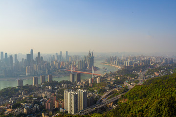 Fototapeta na wymiar Chongqing, China - March 22, 2018: Blurred cityscape in sunset haze. Yangtze River, bridges, ships, central area in the Chinese city of Chongqing. A point is visible in the sky - a plane is flying.
