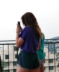 A girl with long brown hair in a purple t-shirt and short gray shorts takes photos on her smartphone of a beautiful landscape on a Sunny summer day.