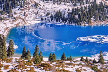 Fototapeta premium Autumn gives way to winter, air temperature drops and water in the lake begins to freeze. Texture and patterns of ice on the serene water surface of a mountain lake; Big Almaty lake in Kazakhstan