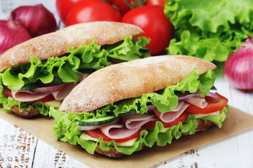 Two sandwiches with fresh vegetables, ham and cheese in ciabatta bread