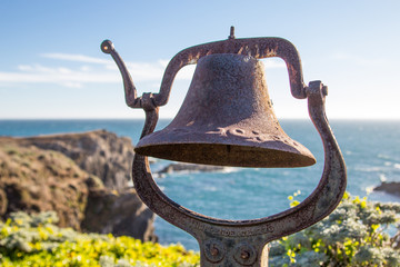 Rusty old nautical brass bell overlooking the pacific ocean coastline.