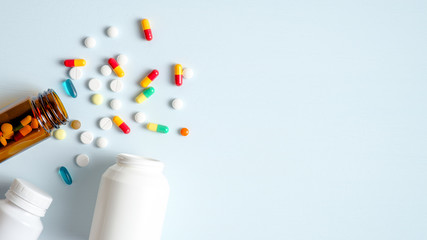 Medical bottles and medication pills spilling out on to pastel blue background. Top view with copy...