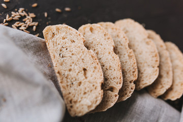 Loaf of fresh sliced baked artisan rye bread on wooden cutting board with knife over dark brown texture background. Top view, copy space.