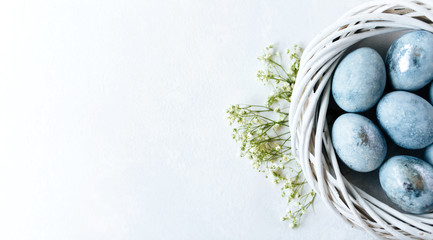 Blue ombre eggs on light background in the white nest. Spring flowers. Daylight. Stylish minimal Compositions in pastel colors. Easter concept. Flat lay, top view. Copy space.