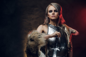 Portrait of a beautiful warrior woman holding a sword wearing steel cuirass and fur. Fantasy fashion. Studio photography on a dark background. Cosplayer as Ciri from The Witcher.