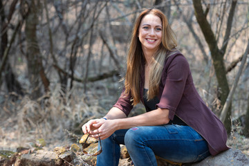 Portrait of a brunet woman with a blue denim and maroon jacket sitting rocks