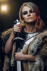 Portrait of a beautiful warrior woman holding a sword wearing steel cuirass and fur. Fantasy fashion. Studio photography on a dark background. Cosplayer as Ciri from The Witcher.