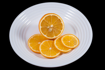 Bright juicy slices of lemon lie on a snow-white plate, with artificial lighting. The element of the vegetarian menu is tropical fruits.