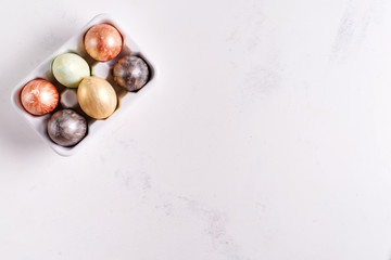 Ceramic egg tray with gold and silver painted Easter eggs on white stone background, holiday concept