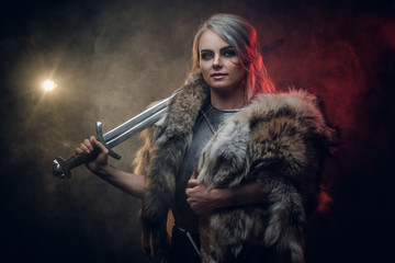 Portrait of a beautiful warrior woman holding a sword wearing steel cuirass and fur. Fantasy fashion. Studio photography on a dark background. Cosplayer as Ciri from The Witcher.