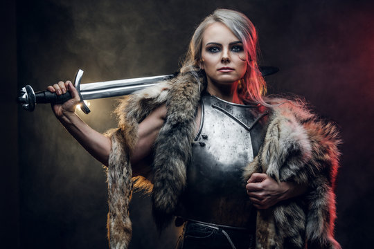 Portrait of a beautiful warrior woman holding a sword wearing steel cuirass and fur. Fantasy fashion. Studio photography on a dark background. Cosplayer as Ciri from The Witcher.