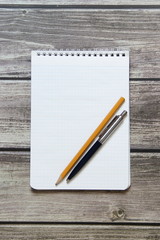 Notepad with a blank white sheet in a checker paper with ball pen and simple graphite pencil lies on the background of wooden boards