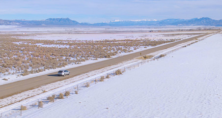 Fototapeta na wymiar DRONE: Flying along a silver car cruising down the empty highway crossing Utah.