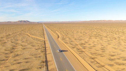 DRONE: Flying behind a silver car as it drives down a highway crossing desert © helivideo