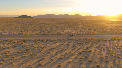 AERIAL: Golden California sunbeams illuminate the landscape for SUV on road trip