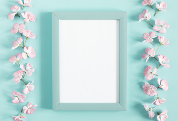 Spring flowers composition. Light pink flowers, empty photo frame on pastel blue background. Wedding. Valentines Day. Mother's day. March 8. Flat lay, top view, copy space