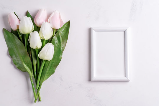 Pastel Tulips with blank picture frame on white marble background, copy space