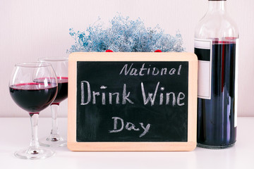 Blackboard with words National Drink Wine Day on the table with wine bottle and two glasses with wine.