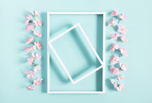 Spring flowers composition. Light pink flowers, empty photo frame on pastel blue background. Wedding. Valentines Day. Mother's day. March 8. Flat lay, top view, copy space