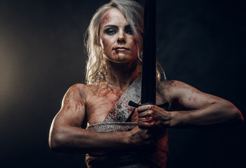 Naked Fantasy woman warrior wearing rag cloth stained with blood and mud posing with a sword. Studio photo on a dark background. Cosplayer as Ciri from The Witcher