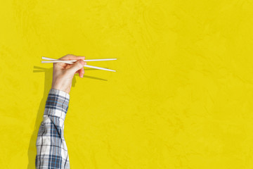 abstract hand holding the empty pair of wooden chopsticks isolated on color background,