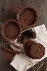 Two cups of hot chocolate with cinnamon on a wooden table with oatmeal cookies and chocolate
