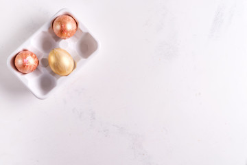 Ceramic egg tray with gold painted Easter eggs on white stone background, holiday concept