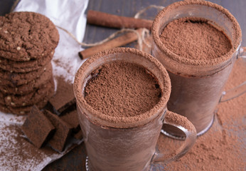 Two cups of hot chocolate on a wooden table with oatmeal cookies and chocolate