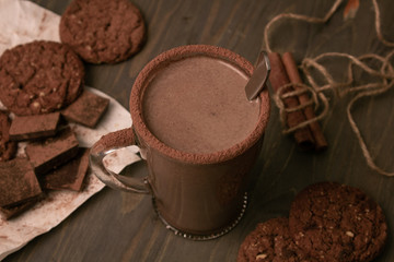 Transparent cup of hot chocolate with cinnamon and milk on a wooden table with oatmeal cookies and chocolate.