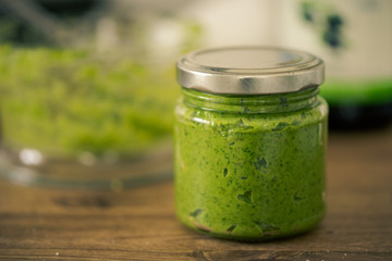 Green pesto in reusable screw-top glass standing on dark wooden table with blurred background
