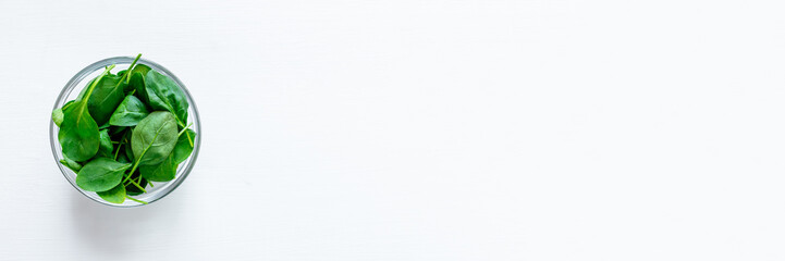 Fresh green spinach leaves in glass bowl on white table. Organic food, healthy diet, vegetarian food. Top view.