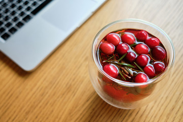 Delicious tea with red berries on a wooden table with a laptop.