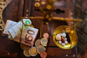 An old scale with money on one side and tablets on the other as a symbol of healthcare costs.