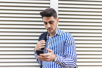Young happy man leaning on house wall while using his smartphone