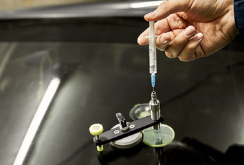 A mechanic uses repair equipment to repair a damaged windshield. It repairs glass chips with an injector under pressure and uses a special polymer.