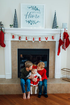 Brothers kissing baby sister in front of Christmas fireplace