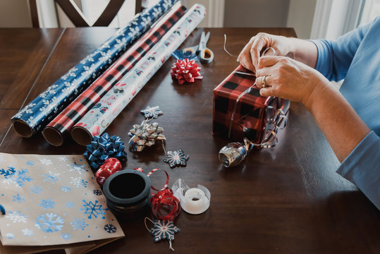 Hands wrapping present with gift wrapping supplies on table.