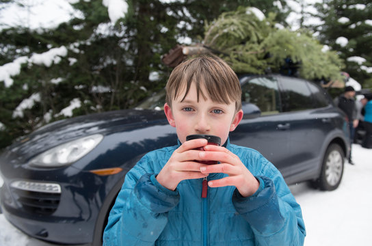 A boy drinks hot chocolate after getting a Christmas tree.