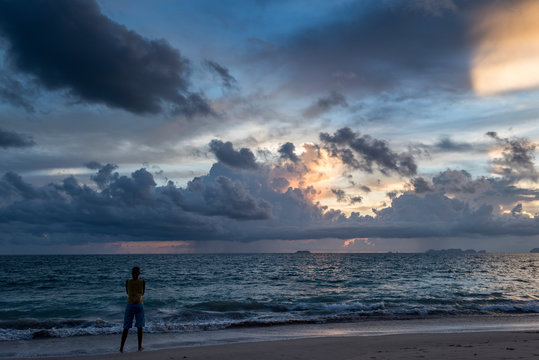 A female traveler observing the sunset in a beach of Koh Lanta island, Thailand.