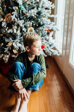 Young boy looking out window next to Christmas tree