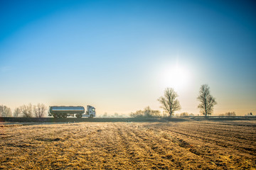 Side view of a gasoline delivery truck driving down a deserted country road on a sunny morning.
