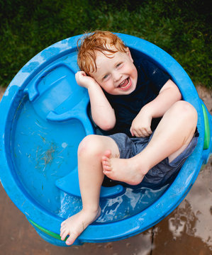 Toddler boy laying in water table with clothes on laughing in backyard