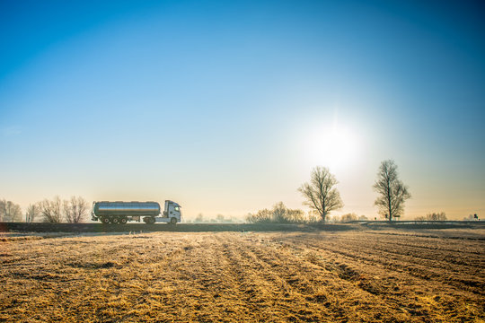 Side view of a gasoline delivery truck driving down a deserted country road on a sunny morning.
