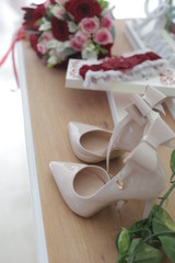 wedding accessories on a dressing table: a bride's bouquet of red and pink roses, women's shoes, a garter of the bride