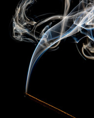A trickle of white smoke from an incense stick on a black background